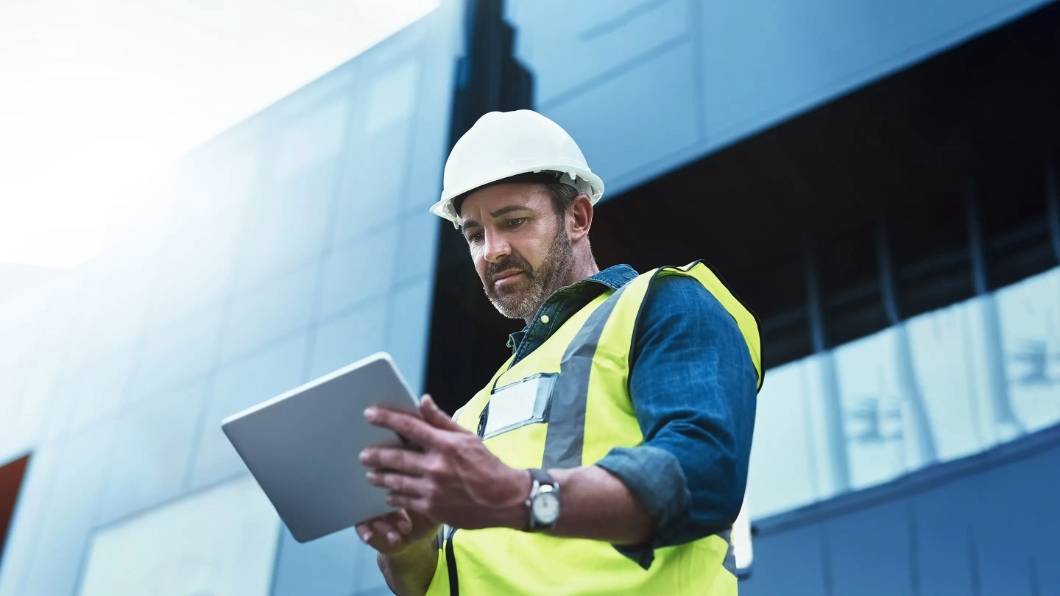 Construction worker in a hard hat and safety vest using a tablet.