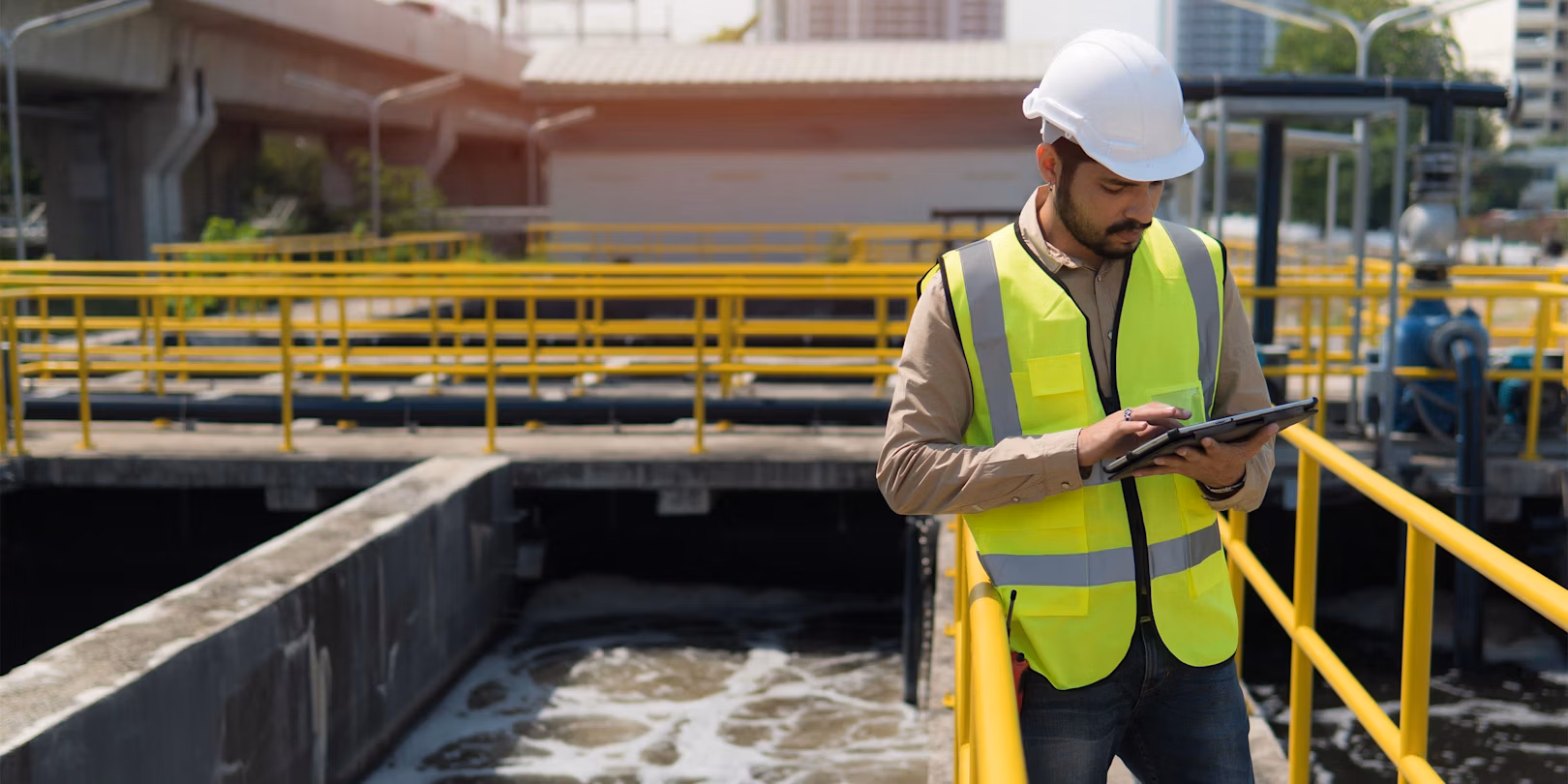 Engineer in safety gear using a tablet at a water treatment facility.
